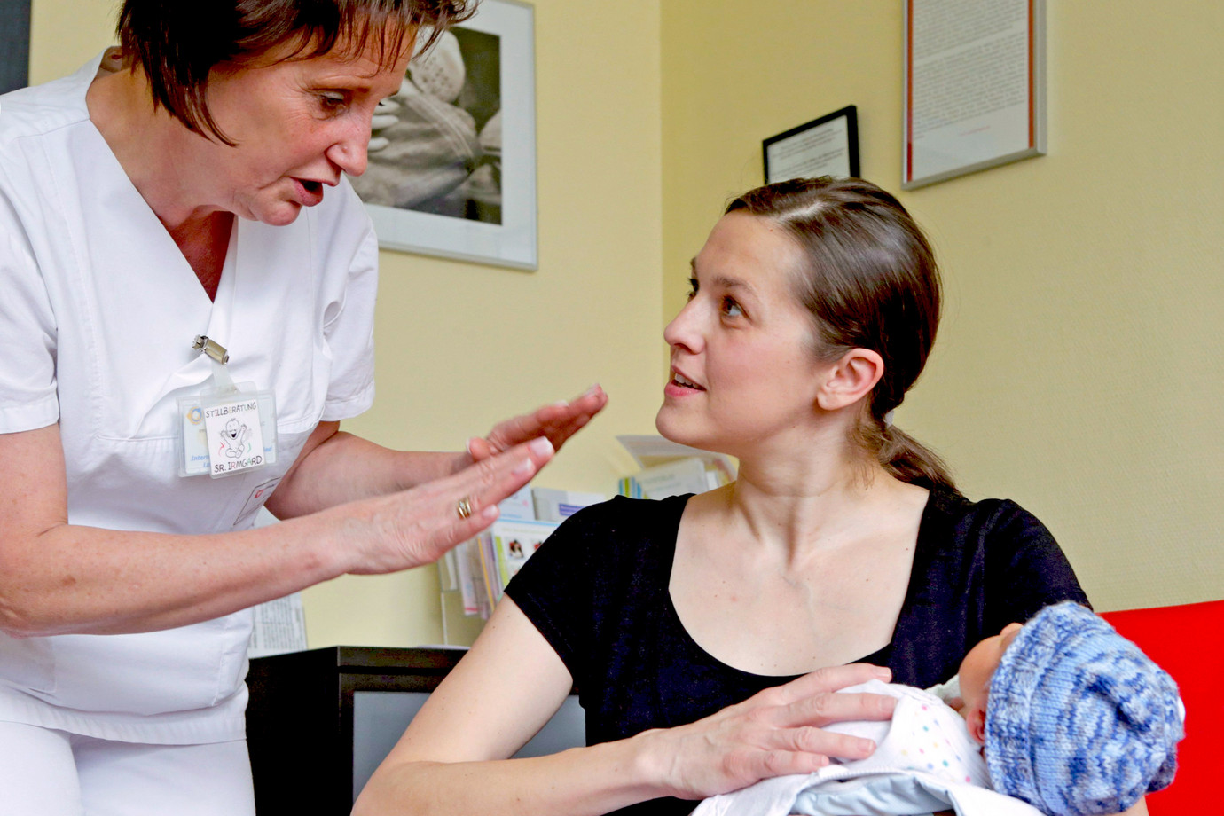 Eine Stillberaterin im Gespräch mit einer Mutter die ihr Neugeborenes auf dem Arm hält